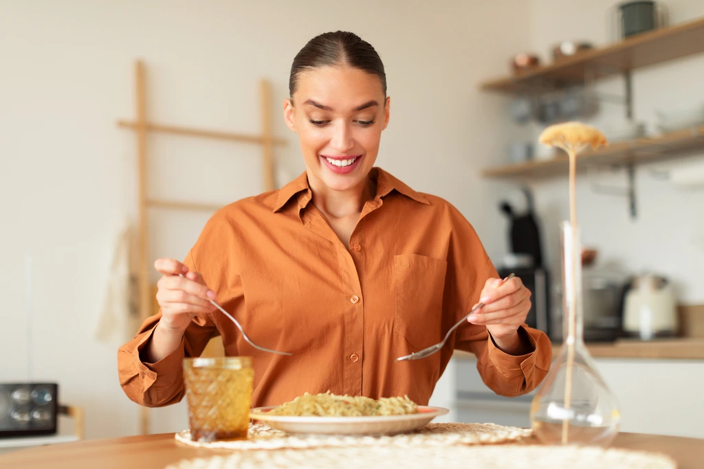 Ava Sinclair, founder of Kitchenican, smiling as she enjoys a plate of homemade pasta in her bright, modern kitchen.