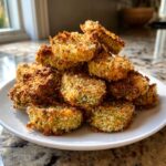 A tall stack of golden brown, breaded Fried Pickles piled high on a white plate.