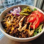 A close-up view of a healthy cheeseburger bowl featuring seasoned ground beef, melted cheese, and special sauce over lettuce.