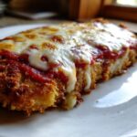 A close-up, appetizing shot of a breaded cutlet covered in marinara sauce and melted mozzarella cheese from the chicken parmesan recipe.
