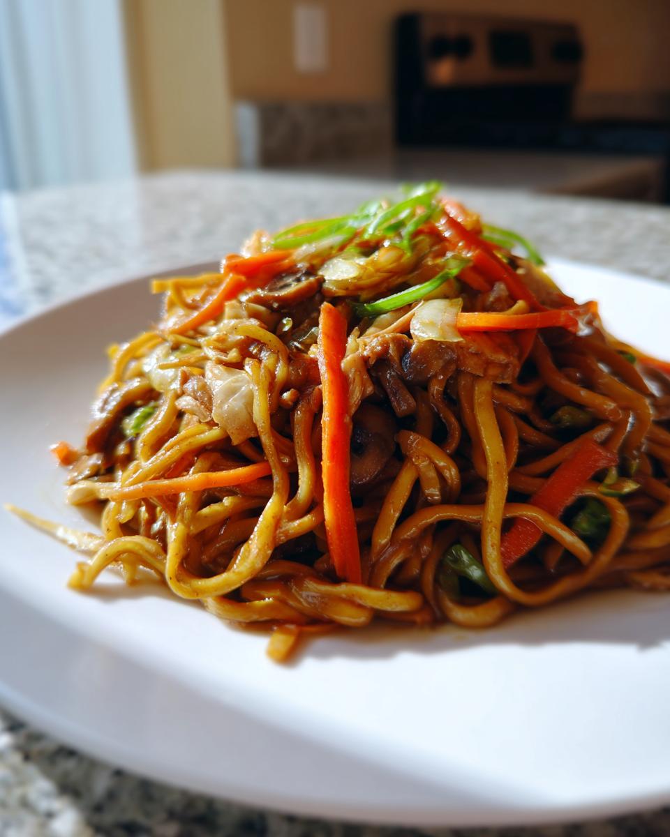 A close-up of a plate piled high with saucy chicken chow mein recipe noodles, shredded carrots, and green onions.