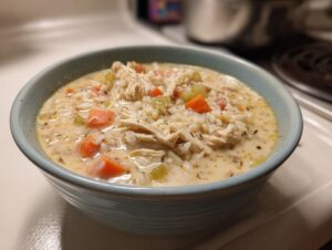 A close-up of a hearty bowl of creamy chicken and wild rice soup, featuring shredded chicken, carrots, and celery.