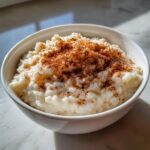 A white bowl filled with creamy rice pudding generously topped with ground cinnamon.