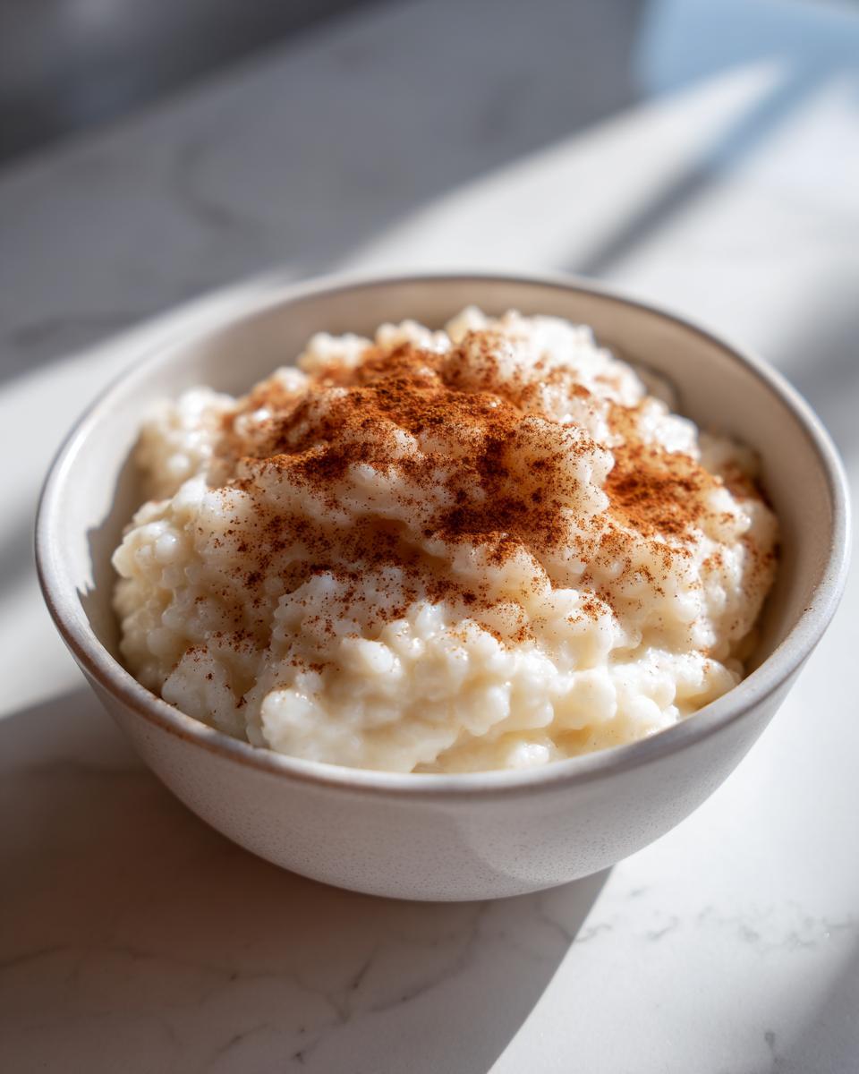 A close-up of creamy rice pudding in a small bowl, generously dusted with ground cinnamon.