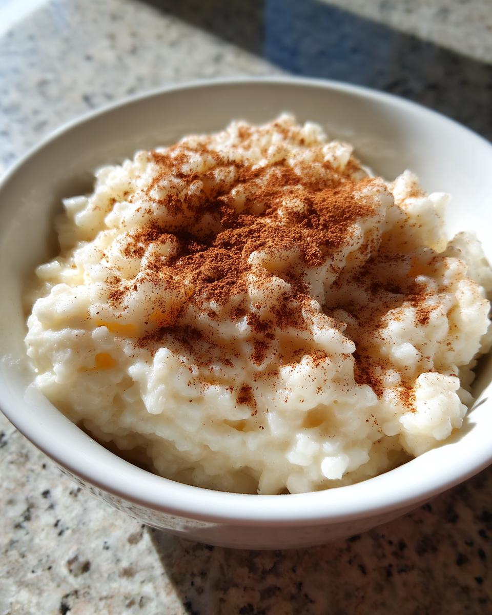 Close-up of creamy rice pudding in a white bowl, generously sprinkled with ground cinnamon.