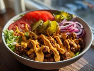 A close-up of a delicious cheeseburger bowl featuring seasoned ground beef, cheese sauce, lettuce, tomato, pickles, and red onion.