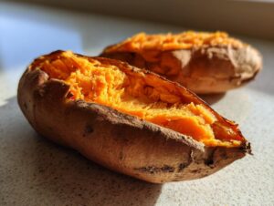 Close-up of a perfectly baked sweet potato split open, revealing its fluffy, bright orange interior.