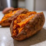 Close-up of a fluffy baked sweet potato split open and sprinkled with coarse salt.