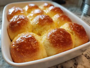 Close-up of twelve golden brown, fluffy dinner rolls glistening with melted butter in a white baking dish.