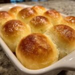 Close-up of twelve golden brown, shiny dinner rolls baked together in a white casserole dish.