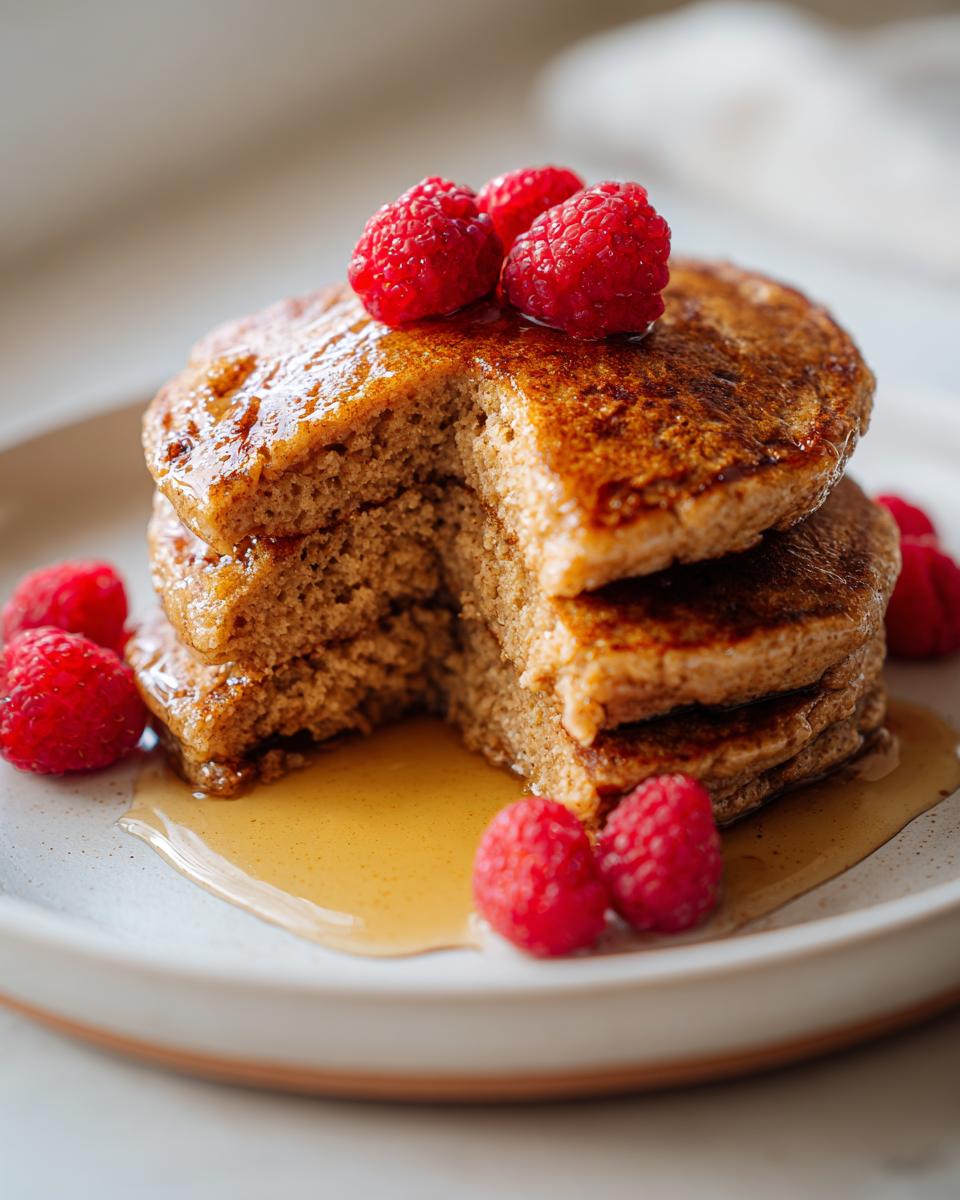 A stack of three fluffy greek yogurt pancakes drizzled with syrup and topped with fresh raspberries.