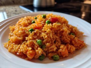 A close-up of fluffy, orange-colored Spanish rice mixed with bright green peas and diced carrots served on a white plate.