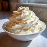 A close-up of perfectly piped, creamy vanilla buttercream frosting piled high in a white bowl.