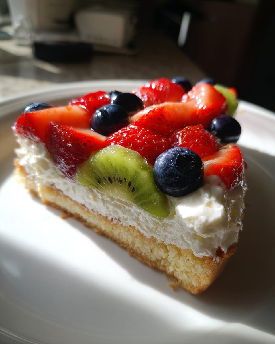 A slice of fruit pizza sugar cookie topped with whipped cream, strawberries, blueberries, and kiwi.