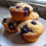 A stack of four golden blueberry muffins topped with coarse sugar crystals.