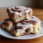 Close-up of three gooey, stacked cinnamon roll pieces generously topped with white cream cheese frosting.