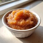 Close-up of chunky, spiced homemade applesauce served in a small white bowl near a window.