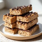 A stack of six homemade chocolate chip protein bars made with oats, topped with mini chocolate chips.