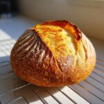A rustic, round loaf of Italian bread with a deeply caramelized, cracked crust resting on a cooling rack.