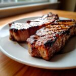 Close-up of two perfectly grilled, caramelized pork steak recipe cuts resting on a white plate.