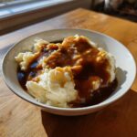 A white bowl filled with fluffy mashed potatoes generously topped with rich, homemade brown gravy.