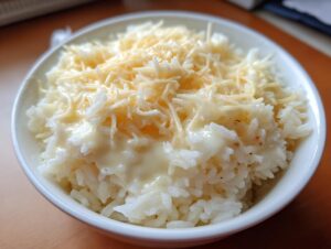 Close-up of a white bowl filled with creamy, cheesy rice topped generously with shredded cheese.