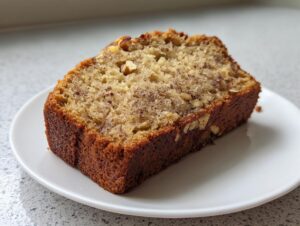 A close-up of a moist slice of sugar free banana bread, featuring visible nuts, on a white plate.