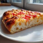 Close-up of a thick slice of pizza made with sourdough discard pizza dough, showing an airy, open crumb structure and browned crust.