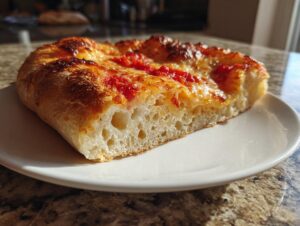 Close-up of a thick slice of pizza made with sourdough discard pizza dough, showing an open, airy crumb structure.