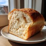A freshly baked loaf of sourdough sandwich bread, sliced open to show the soft, airy crumb, resting on a white plate.