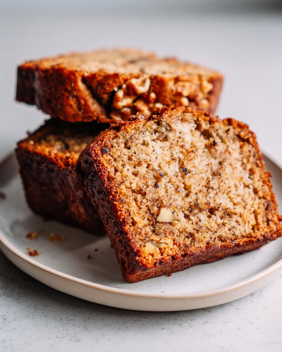 Close-up of three stacked slices of moist sugar free banana bread with visible walnuts on a light plate.