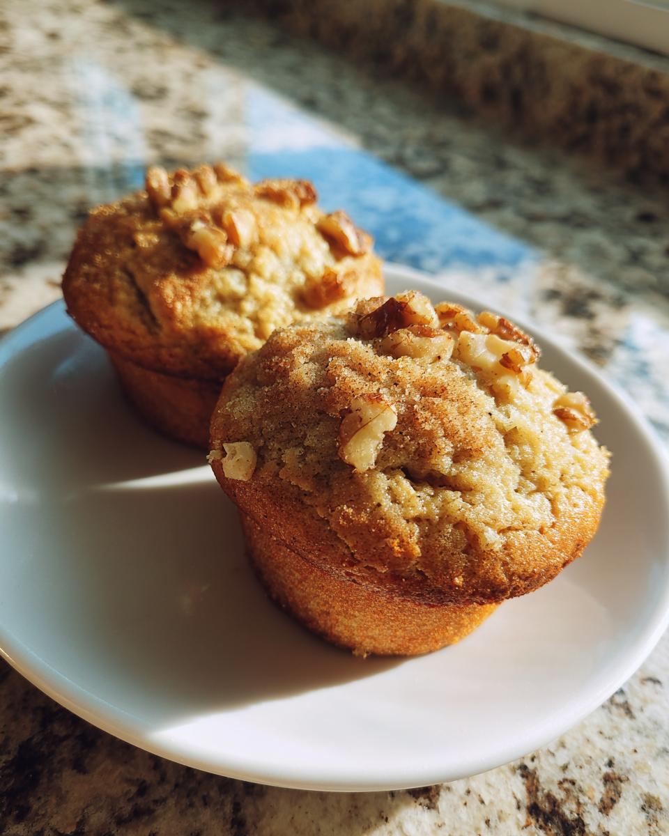 Close-up of two freshly baked banana nut muffins topped with walnuts, sitting on a white plate.