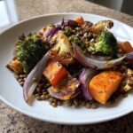 Close-up of a hearty veggie lentil salad featuring roasted sweet potato, broccoli, cauliflower, and red onion over brown lentils.