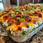 A close-up view of a fully assembled 7 layer salad topped with shredded cheese, bacon, and green onions.