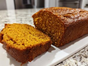 A freshly baked loaf of moist pumpkin bread, with one thick slice cut and resting beside it.