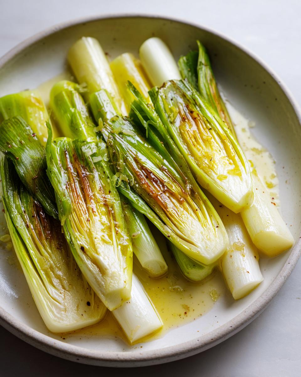 Close-up of tender, halved braised leeks swimming in a pool of melted butter or dressing.