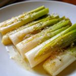 Close-up of tender, bright green and white braised leeks topped with a glistening garlic and herb sauce.