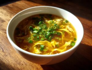 Close-up of a white bowl filled with golden egg drop soup, garnished with fresh green onions.