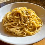 A close-up of creamy spaghetti coated in sauce, representing amazing parmesan pasta, topped generously with black pepper.