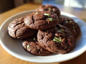 A stack of rich, dark chocolate Andes Mint Cookies featuring visible green mint pieces on a white plate.