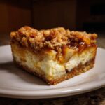 A single serving of rich apple cheesecake bars featuring a creamy layer, apple filling, and thick crumb topping.
