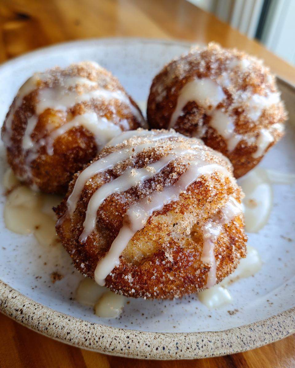 Three golden brown baked apple fritters coated in cinnamon sugar and drizzled with vanilla glaze.