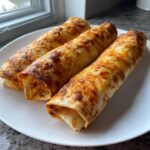 Three golden brown Baked Chicken Chimichangas topped with melted, slightly browned cheese, served on a white plate.