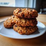 A stack of three freshly baked banana oatmeal cookies studded with chocolate chips sitting on a white plate.