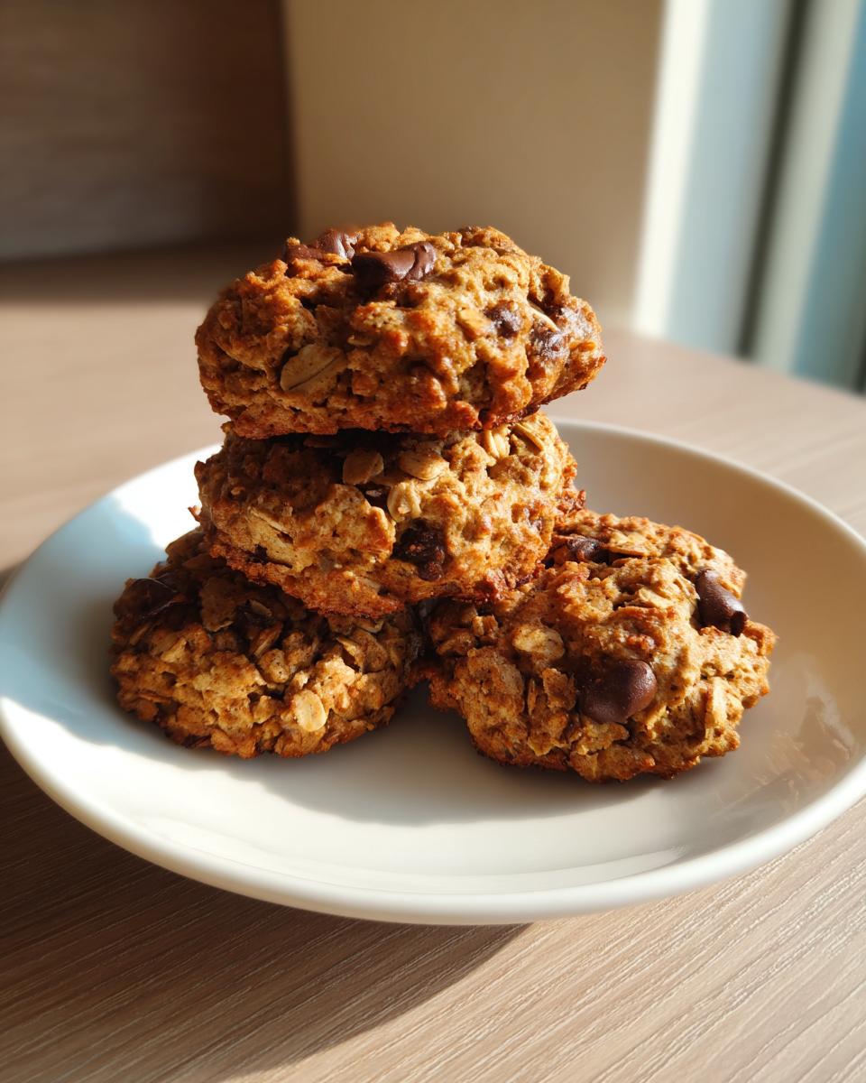 A stack of four golden brown banana oatmeal cookies with visible chocolate chips on a white plate.