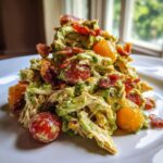 A serving of creamy BLT chicken salad mixed with avocado dressing, bacon bits, and whole cherry tomatoes.