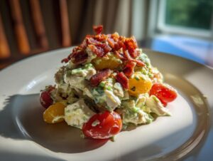 A mound of creamy BLT chicken salad mixed with cherry tomatoes and topped generously with crispy bacon bits.