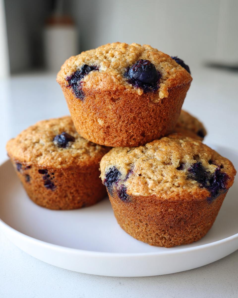 A stack of three golden-brown blueberry oatmeal muffins sitting on a white plate.