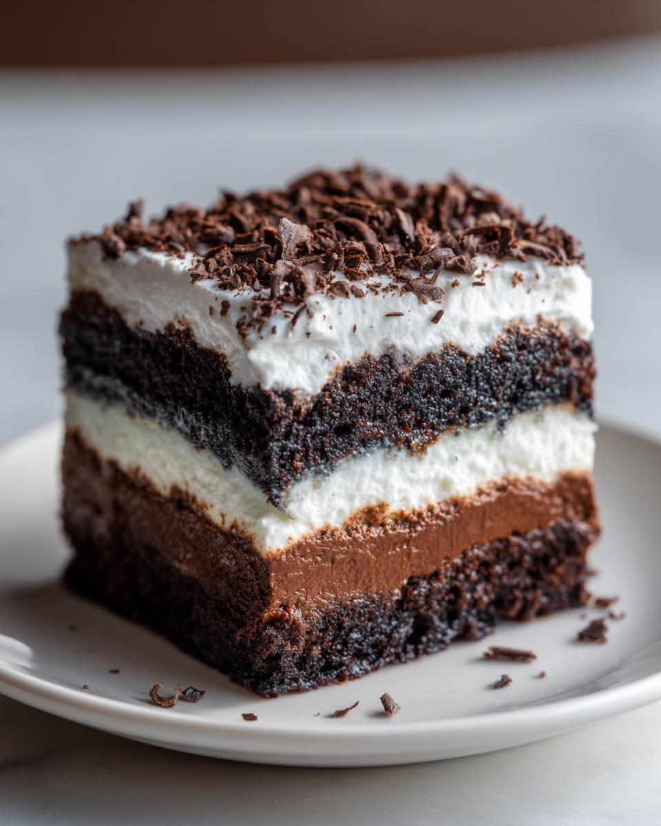 Close-up of a rich slice of brownie refrigerator cake showing layers of dark cake, chocolate mousse, and white cream, topped with chocolate shavings.