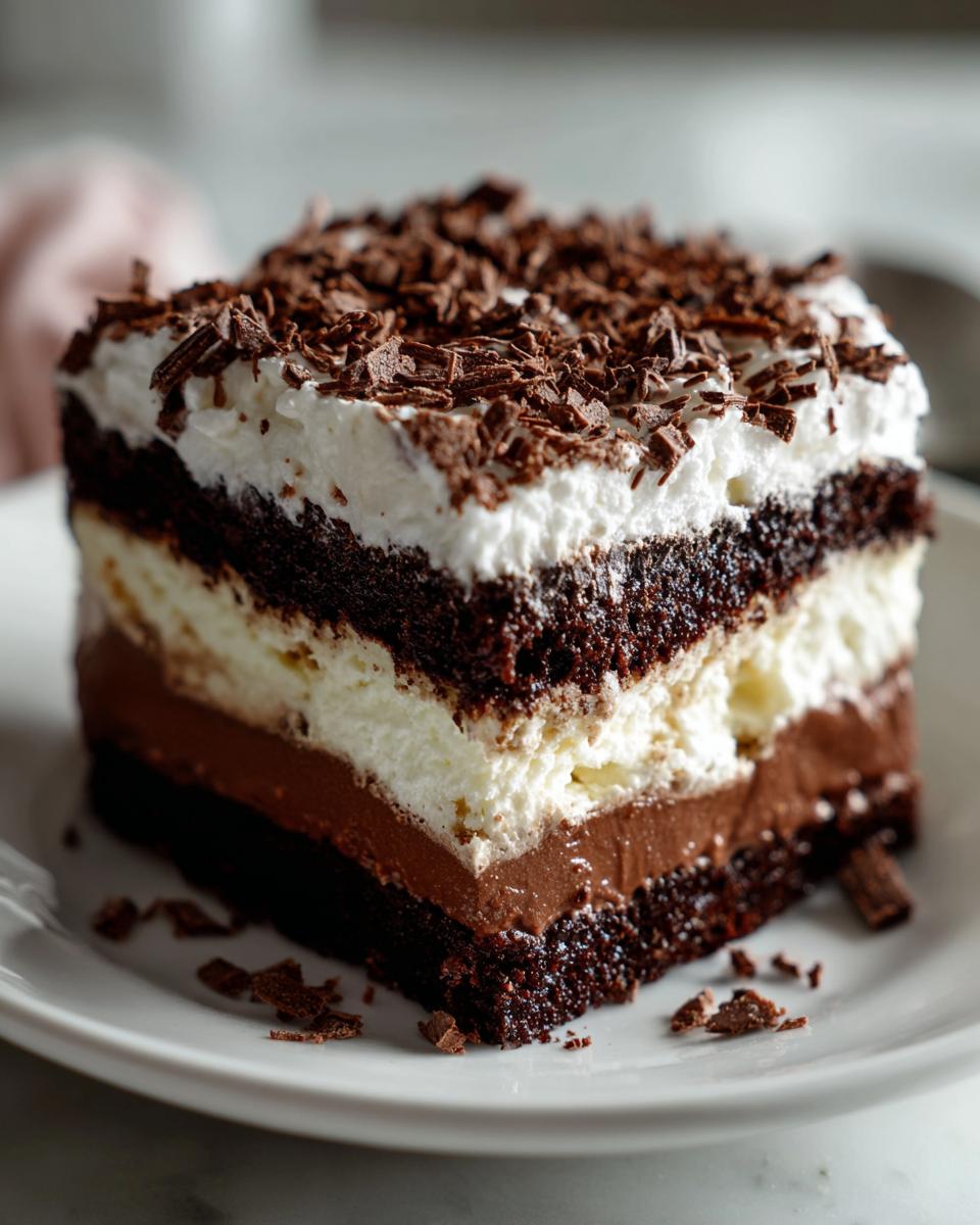 A decadent slice of brownie refrigerator cake featuring layers of dark chocolate cake, creamy filling, and topped with whipped cream and chocolate shavings.